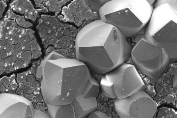 Cristais de carbonato de ferro (FeCO3) precipitados sobre camada de produto de corrosão craquelado formado sobre o aço UNS K41245 grau T5 (5 % Cr) sob exposição em meio de NaCl/CO2 (Sweet Corrosion). Imagens obtidas por elétrons secundários em microscópio eletrônico de varredura