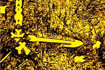 Imagem do IPT que integra a mostra é de uma liga metálica 1,5%C,  5Nb, 2%Mo, 2%W, 1%V. A seta, que é um carboneto, indica um contorno de grão. A matriz é formada de martensita e austenita retida. A ausência da adição do titânio nesta liga evidencia uma morfologia do carboneto de nióbio não satisfatória para as propriedades mecânicas e de resistência ao desgaste da liga.