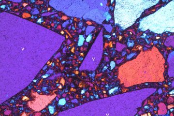 Fotomicrografia da 'superfície de quartzo'. Os fragmentos de vidro estão indicados com a letra 'v', e a face esquerda do menor fragmento (centro da foto) apresenta metalização