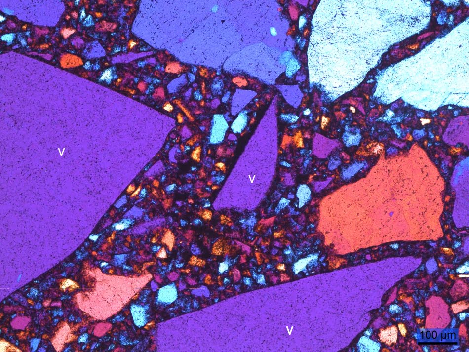 Fotomicrografia da \'superfície de quartzo\'. Os fragmentos de vidro estão indicados com a letra \'v\', e a face esquerda do menor fragmento (centro da foto) apresenta metalização