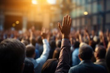 Grupo de pessoas desfocadas com a mão levantada. Imagem gerada por IA.